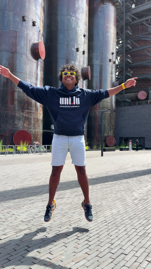 Aswin Lutchanah jumping in a University of Luxembourg hoodie in front of the Belval blast furnaces