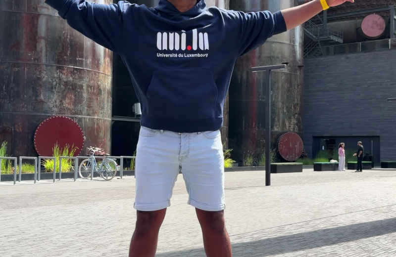 Aswin Lutchanah jumping in a University of Luxembourg hoodie in front of the Belval blast furnaces
