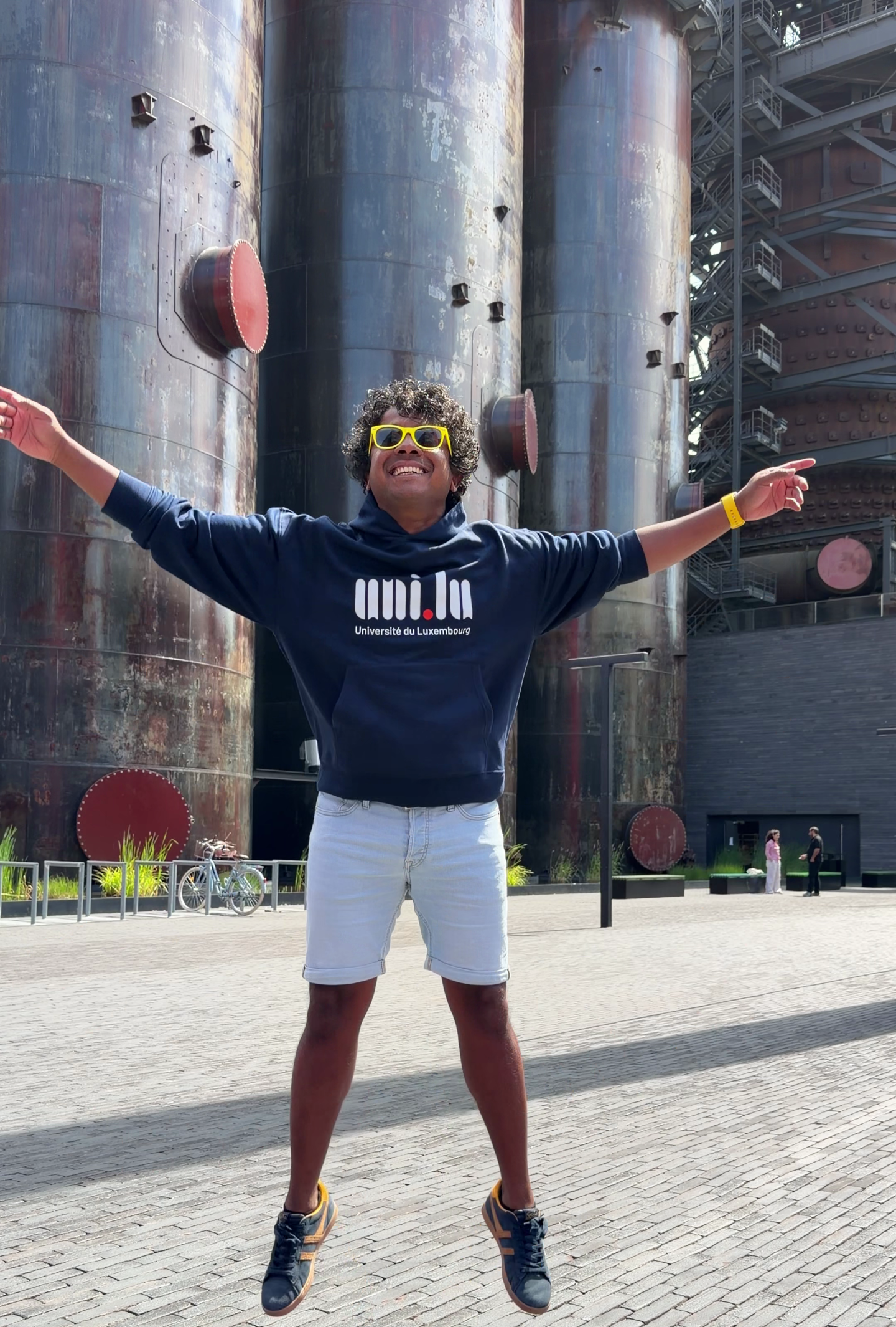 Aswin Lutchanah jumping in a University of Luxembourg hoodie in front of the Belval blast furnaces