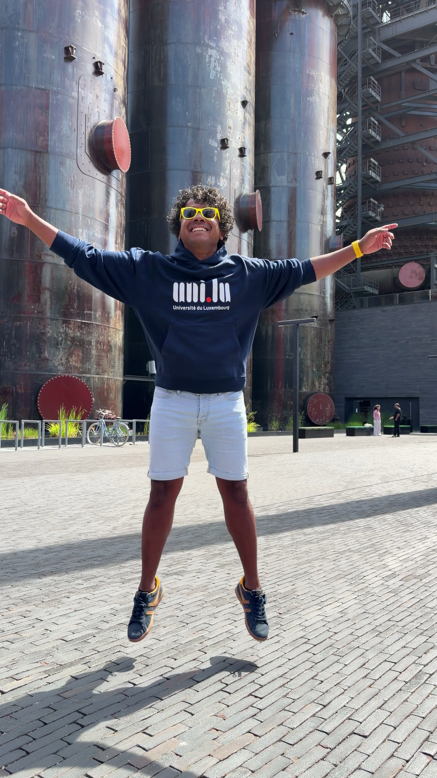 Aswin Lutchanah jumping in a University of Luxembourg hoodie in front of the Belval blast furnaces