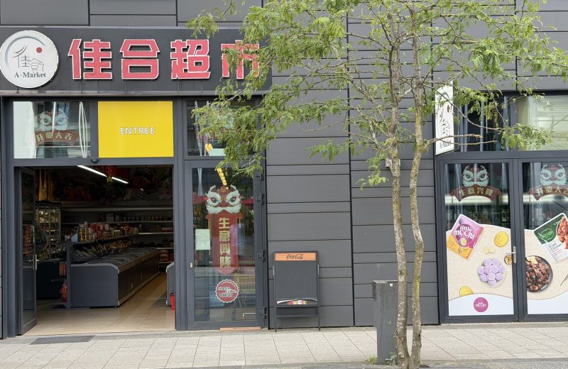 The A-Market Asian supermarket on avenue du Swing in Belval, its red Chinese lettering and A-Market sign above an open entrance, with chest freezers and shelves visible inside.