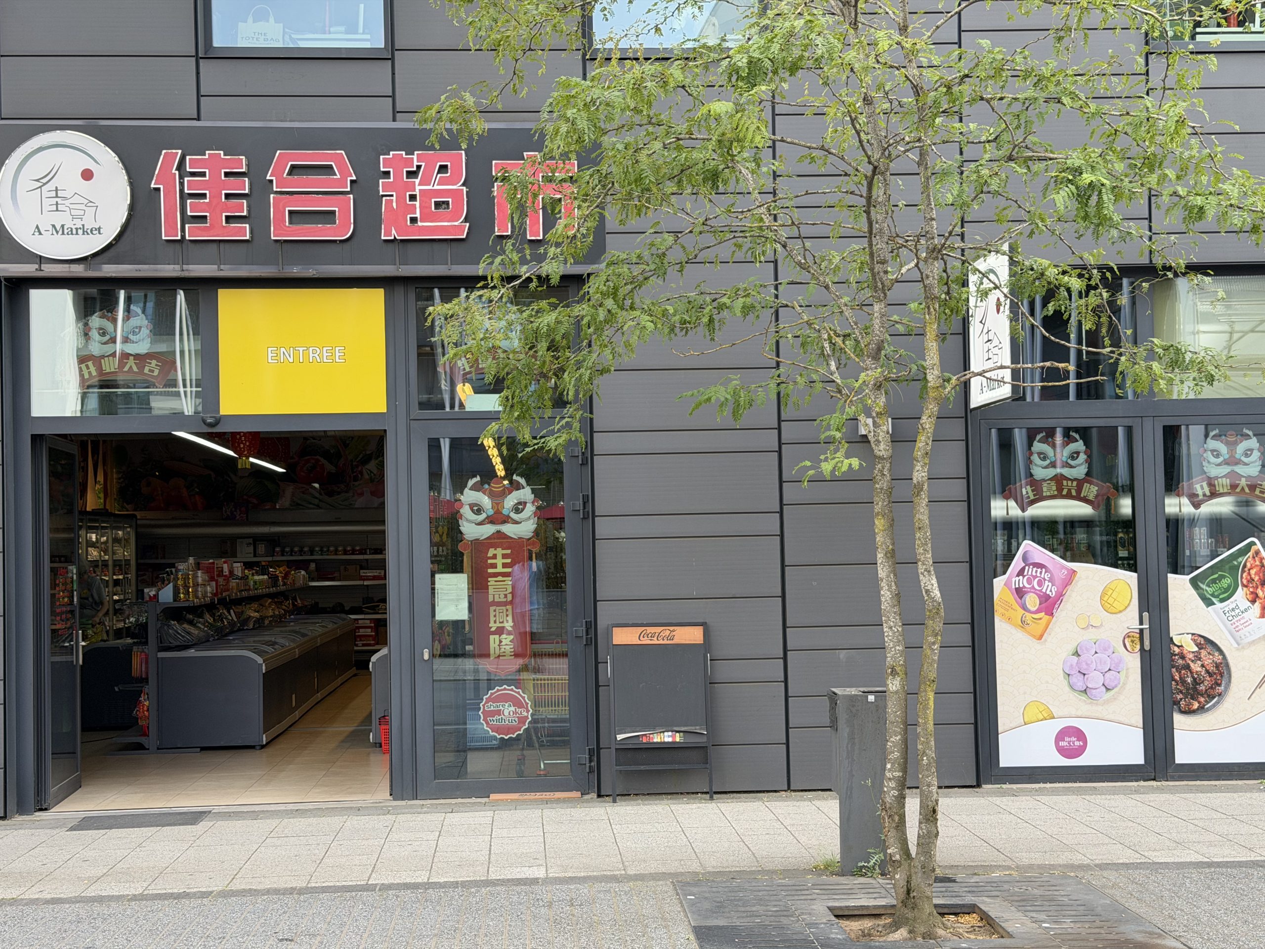 The A-Market Asian supermarket on avenue du Swing in Belval, its red Chinese lettering and A-Market sign above an open entrance, with chest freezers and shelves visible inside.