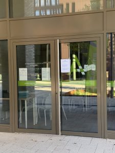 The glass entrance of Auto-École A Plus in Belval, with the green A Plus logo, a closed sign and a notice taped to the door listing theory class times in French, Luxembourgish and English.
