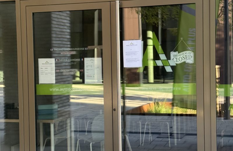 The glass entrance of Auto-École A Plus in Belval, with the green A Plus logo, a closed sign and a notice taped to the door listing theory class times in French, Luxembourgish and English.