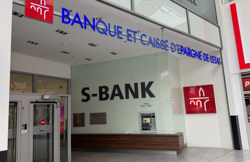 The S-BANK and BCEE branded frontage of the Spuerkeess bank branch at Belval Plaza (shown mirrored in the photograph, shot through glass), with the Spuerkeess wordmark above the entrance.
