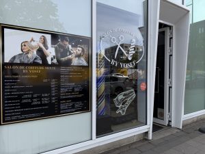 The By Yosef salon in Belval, with a large price board in French and English in the window and the salon logo etched on the glass.