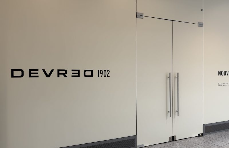 The hoarding around the future Devred 1902 unit in Belval Plaza II, a pale panel carrying the black DEVRED 1902 wordmark beside glass doors, with the brand's own text panel to the right.
