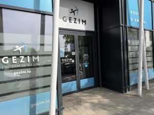 The GEZIM employment agency entrance in Belval, with the company name and the strapline l'intérim de A à Zen on the glass and opening hours on the door.