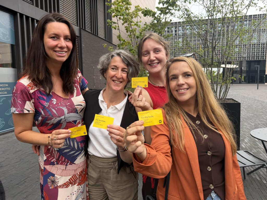 Four guests holding up yellow icebreaker cards reading The Kind Word, The Sunshine, The Good Morning and The Big Smile, all from the same theme, The Good Vibes.