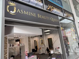 The Jasmine Beauty Queen salon window at Belval Plaza, with a printed price board listing haircuts, colour and styling services and prices visible through the glass.