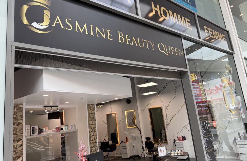 The Jasmine Beauty Queen salon window at Belval Plaza, with a printed price board listing haircuts, colour and styling services and prices visible through the glass.