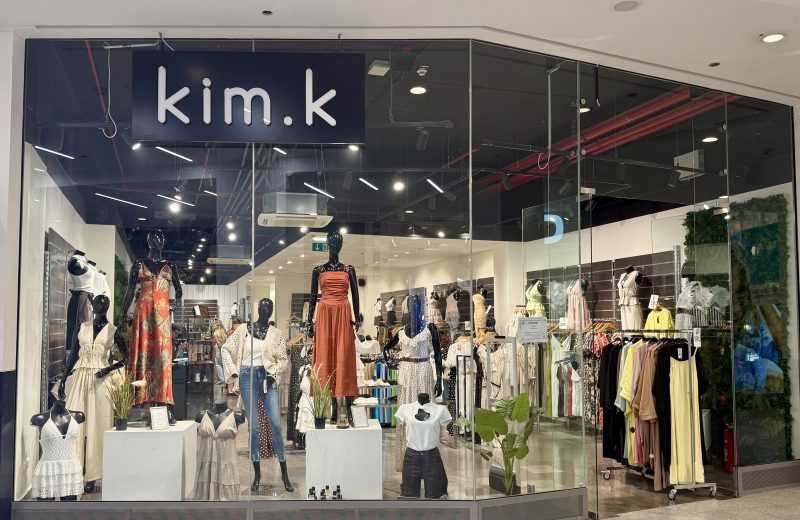 The kim.k shopfront in Belval Plaza, with the navy kim.k sign above the entrance and mannequins dressed in printed dresses, denim and knitwear in the window display.