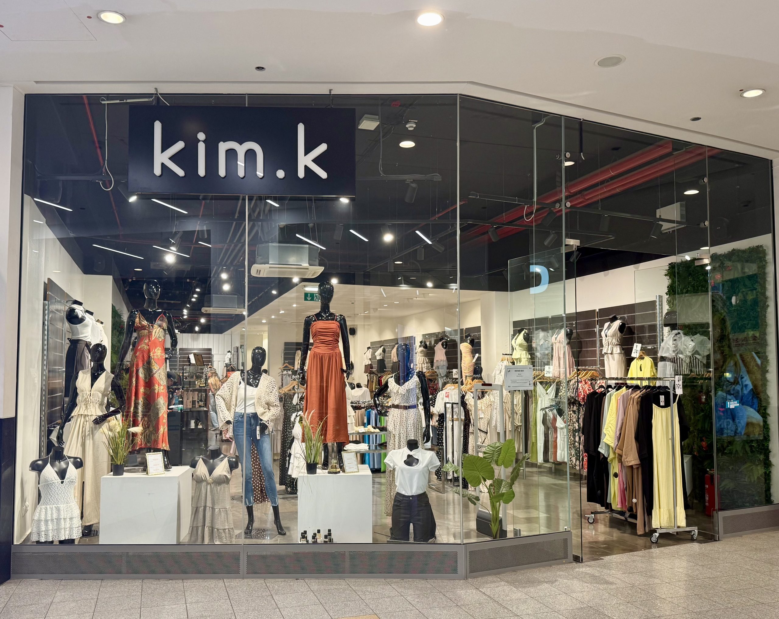 The kim.k shopfront in Belval Plaza, with the navy kim.k sign above the entrance and mannequins dressed in printed dresses, denim and knitwear in the window display.