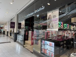La Boutique du Coiffeur shopfront at Belval Plaza II, dark storefront with "La Boutique du Coiffeur" lettering, shelves of Schwarzkopf Professional haircare products, and a banner advertising twenty per cent off two products purchased together.