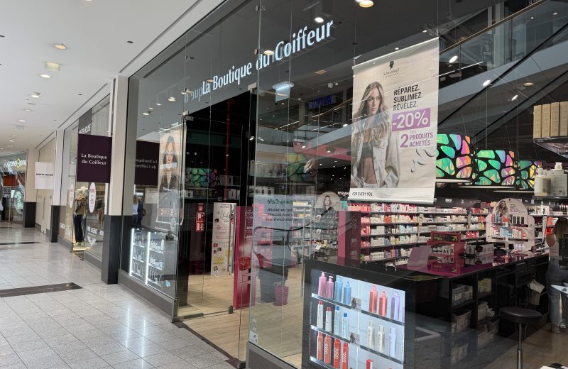 La Boutique du Coiffeur shopfront at Belval Plaza II, dark storefront with "La Boutique du Coiffeur" lettering, shelves of Schwarzkopf Professional haircare products, and a banner advertising twenty per cent off two products purchased together.