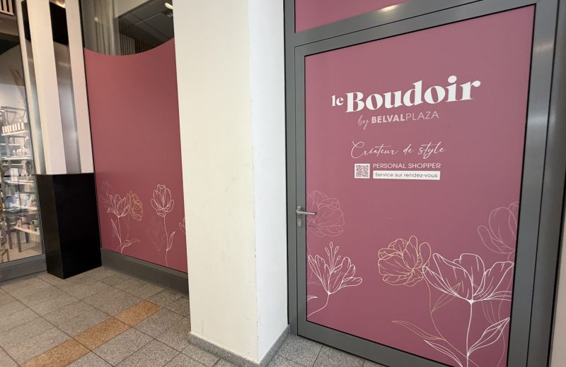 The Le Boudoir by Belval Plaza door, a deep rose pink panel with white "le Boudoir" script lettering, "by BELVAL PLAZA" underneath, "Créateur de style" in a handwritten font, a QR code and "PERSONAL SHOPPER, Service sur rendez-vous" text, and gold line-drawn floral illustrations across the lower half of the door and the wall beside it.