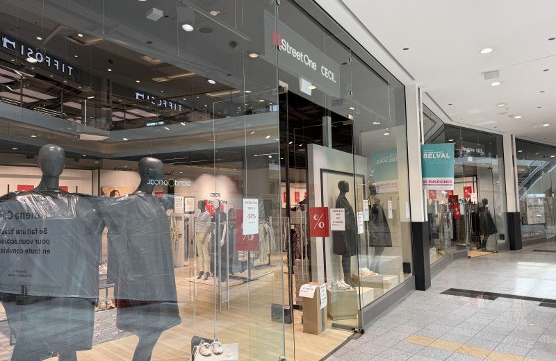 Street One CECIL shopfront at Belval Plaza, grey storefront with the Street One and CECIL logos side by side above the door, mannequins in autumn clothing, red clearance percentage signs on the glass, and a teal "Belval Plaza, 80 enseignes" poster in the window.