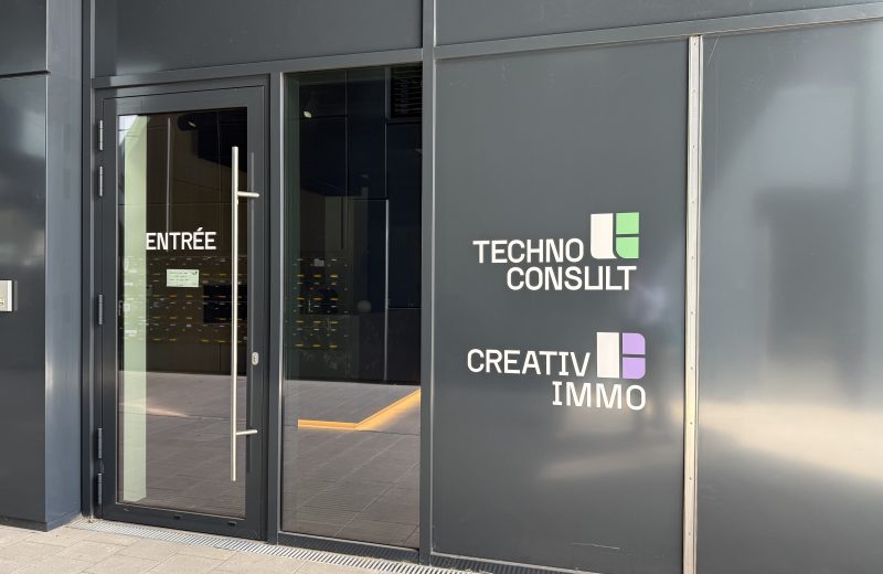 The shared entrance to Résidence Gateway on boulevard du Jazz, a grey panelled frontage with a glass door marked ENTRÉE opening onto a wall of letterboxes, and the Techno Consult and Creativ Immo logos applied to the panel beside it.