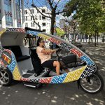The Vëlodukt Ride bike taxi parked outside MediaMarkt in Belval, its driver seated at the handlebars