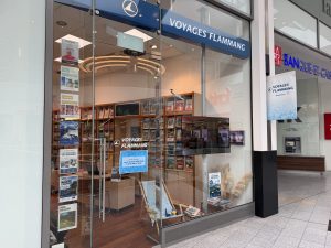 The Voyages Flammang shopfront at Belval Plaza, with the Flammang wordmark above the entrance and a printed poster in the window giving opening hours for Monday to Friday and Saturday.