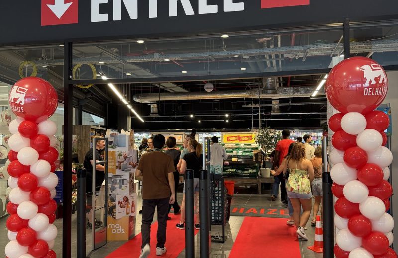 The entrance to Delhaize Belval on reopening morning, with a red carpet, red and white balloon columns either side and shoppers walking in under the Entrée sign