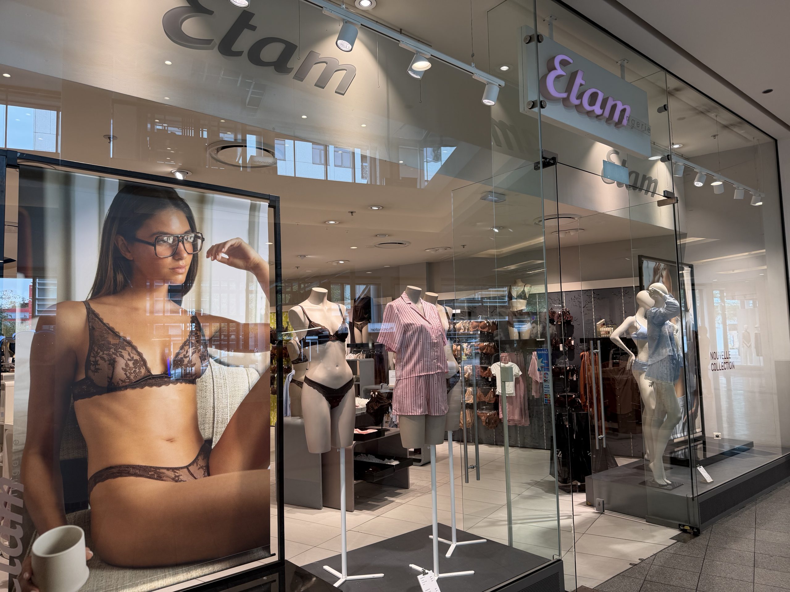 The Etam shopfront in Belval Plaza, with a large window photograph of a model in lace lingerie beside the entrance and mannequins dressed in striped pyjamas and lace tops inside.