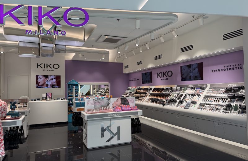 The Kiko Milano shopfront in Belval Plaza, with the purple KIKO MILANO sign above the entrance and rows of makeup testers lining the wall inside, including a table of new lipstick launches.