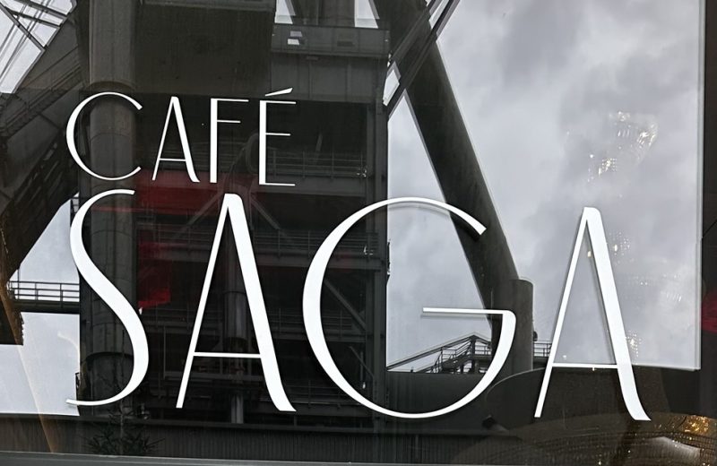 The Café Saga sign on the glass front, with the Belval blast furnace reflected in the window.
