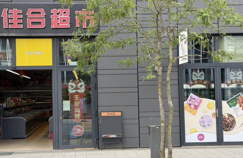 The A-Market Asian supermarket on avenue du Swing in Belval, its red Chinese lettering and A-Market sign above an open entrance, with chest freezers and shelves visible inside.
