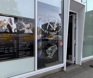 The By Yosef salon in Belval, with a large price board in French and English in the window and the salon logo etched on the glass.