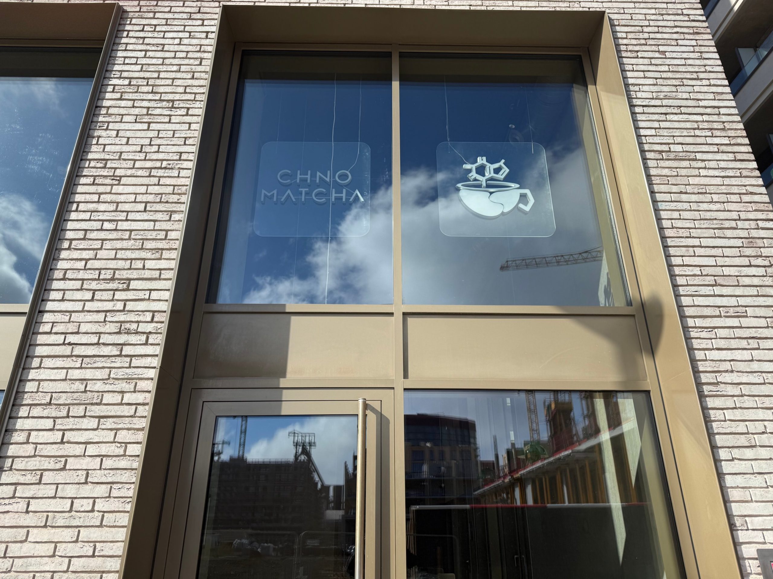 The frosted window of Chno Matcha in Belvaux, with the wordmark and a logo of a cup below a molecule.