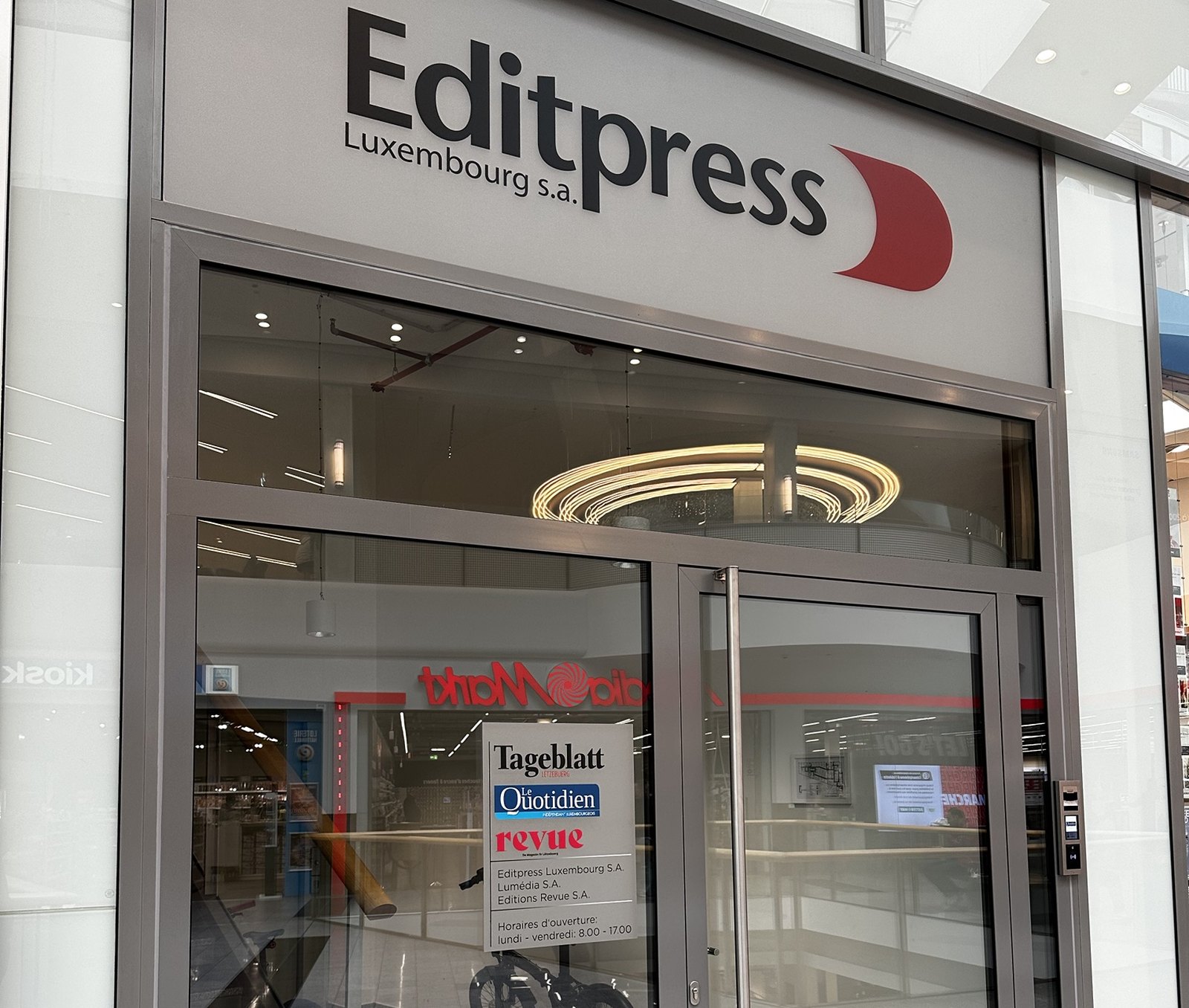 Entrance to the Editpress Luxembourg offices on the upper level of Belval Plaza, with the Editpress fascia above the door and a plate listing Tageblatt, Le Quotidien and Revue.