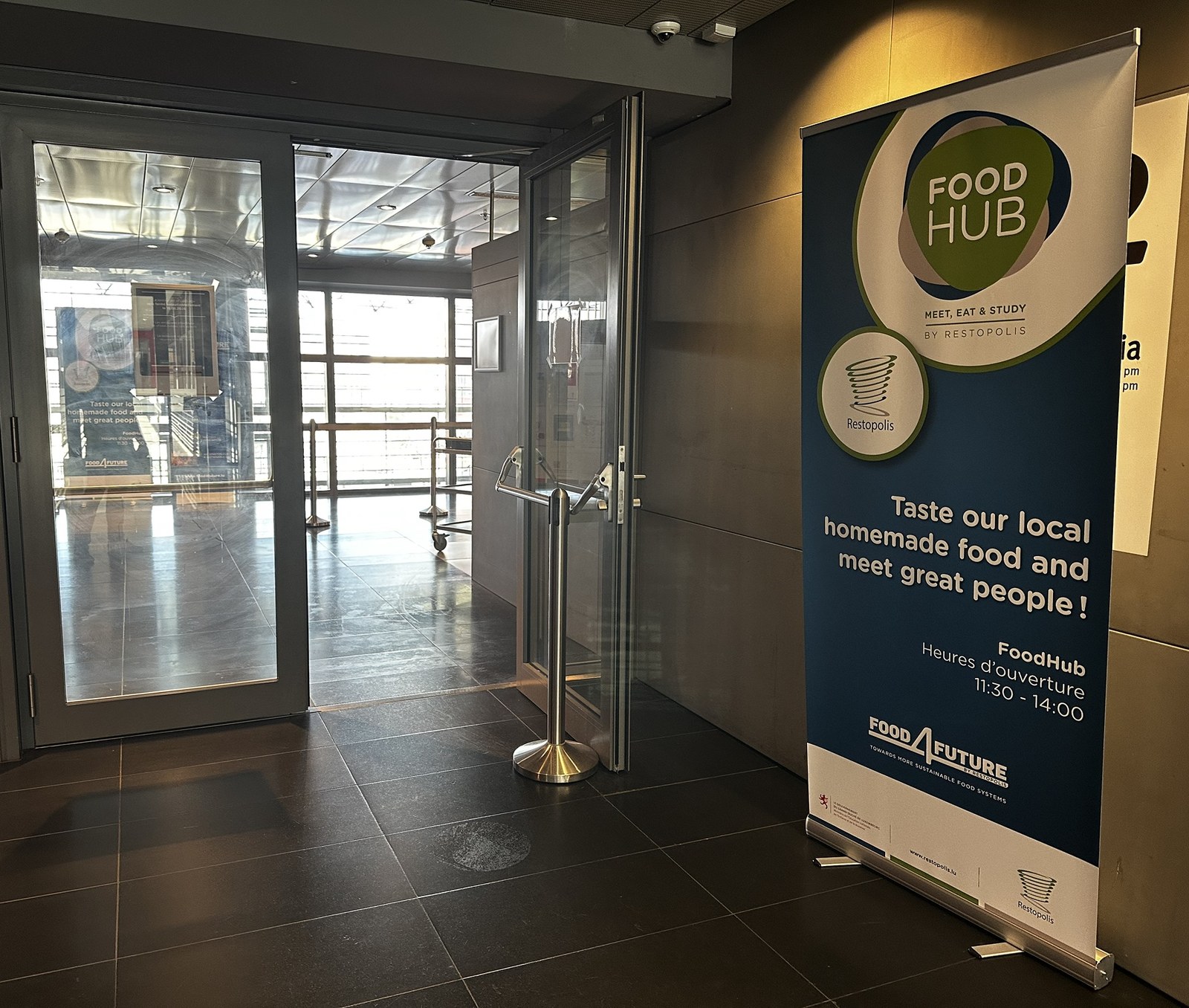 The Food Hub entrance in the Terres Rouges building, a roll-up banner beside the open doors giving the name, the Restopolis mark and the 11:30 to 14:00 opening hours.