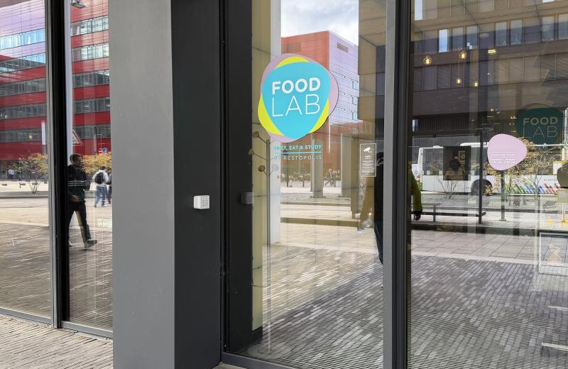 The Food Lab entrance at the Maison des Sciences Humaines, the pink, cyan and yellow Food Lab roundel on the glass door with MEET, EAT & STUDY by Restopolis beneath it.