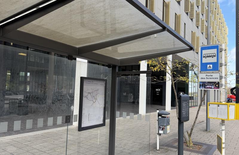 The Porte des Sciences bus shelter in Belval, its network map and real-time display beside the stop sign, with the Maison des Sciences Humaines behind.