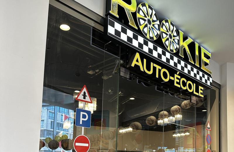 The Rookie Auto-École shopfront in Belval Plaza II, a yellow and black fascia with two wheel trims in place of the double O, road signs in the window and a classroom of yellow chairs inside.